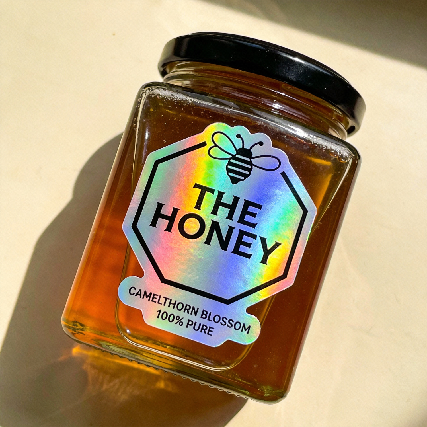 Jar of honey with a custom colorful holographic label on a beige background