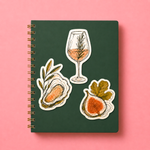 Illustrated artist stickers of a wine glass oyster and fig on a green notebook