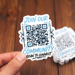 A hand holding a custom die-cut vinyl sticker featuring a QR code, with the text 'JOIN OUR COMMUNITY' and 'SCAN TO CONNECT' in a light blue and black color scheme.