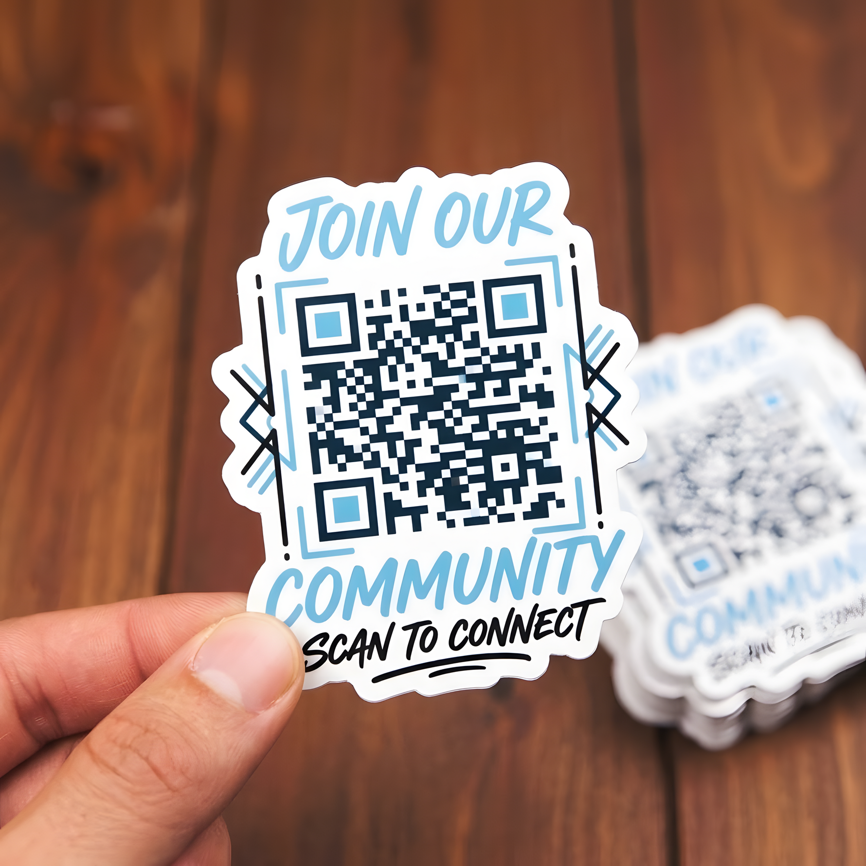 A hand holding a custom die-cut vinyl sticker featuring a QR code, with the text 'JOIN OUR COMMUNITY' and 'SCAN TO CONNECT' in a light blue and black color scheme.