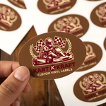 Hand holding a red and brown kart racing themed vinyl sticker with a racer and victory checkered flags.