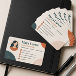 A stack of rounded rectangle matte vinyl business card stickers for a creative consultant, arranged on a black leather journal next to two metallic pens, captured in clean natural daylight.