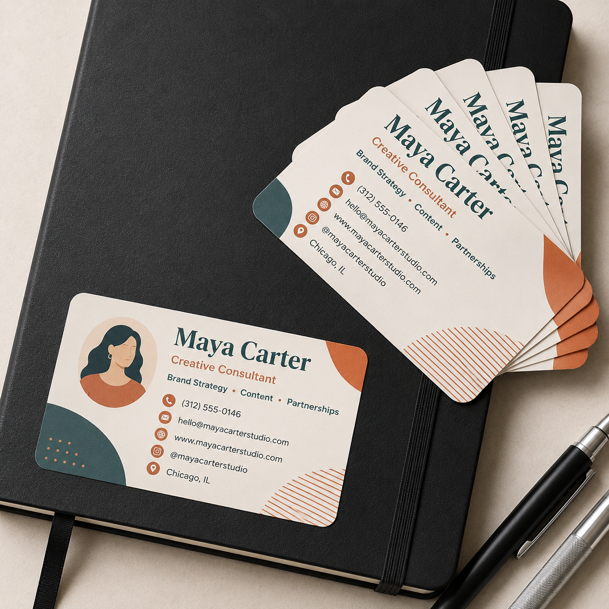 A stack of rounded rectangle matte vinyl business card stickers for a creative consultant, arranged on a black leather journal next to two metallic pens, captured in clean natural daylight.