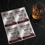 Custom metallic silver vinyl whisky label sheets displayed beside a glass of whisky with ice on a black marble surface.