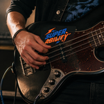 A musician playing a black electric guitar decorated with a custom band sticker featuring typography.