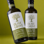 Custom waterproof labels with olive grove extra virgin oil design applied on glass olive oil bottles with water droplets.
