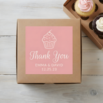 Personalized pink cupcake thank you sticker on a kraft bakery box beside cupcakes.