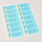 A full sheet of personalized light blue rectangular labels with elegant botanical illustrations and business address text.