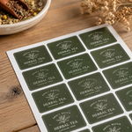Personalized green vinyl labels for small batch herbal tea packaging on a rustic wooden background.