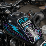 A person in black gloves applying a 'Play Mode' gaming vinyl decal to a black motorcycle gas tank, featuring neon purple and blue pixel art and controller graphics.