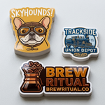 Stacks of premium glossy vinyl stickers featuring various brand logos like "Skyhounds" and "Brew Ritual" showing material thickness.