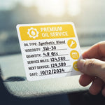 Hand holding a custom yellow premium oil service sticker detailing oil type and mileage.