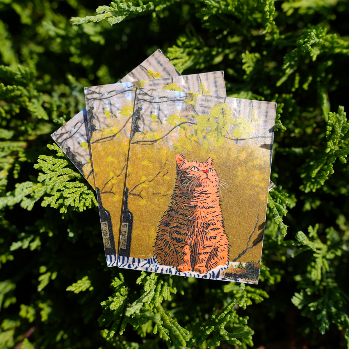 A stack of rectangle stickers featuring an artistic illustration of an orange tabby cat sitting among yellow foliage, placed on green leaves