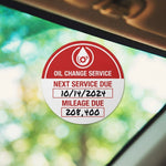 Round custom oil change service reminder sticker with gear icon on a vehicle windshield.