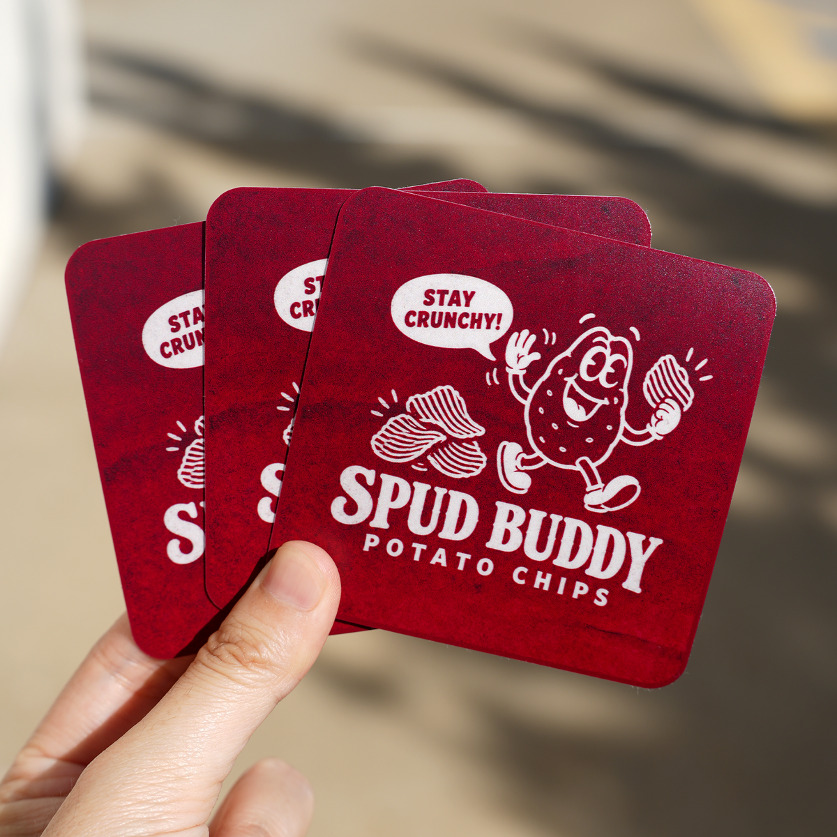 A hand displaying dark red rounded rectangle stickers with a potato chips cartoon branding design, perfect for rounded corner rectangle stickers
