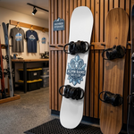 Snowboard with ski club custom sticker displayed on wooden indoor wall rack in snowboard shop interior