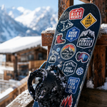 Snowboard with waterproof custom stickers leaning on wooden railing at ski resort with mountain background