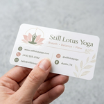 A close-up of a hand holding a rectangular glossy vinyl business card sticker with rounded corners, featuring a sleek reflective finish and a clean lotus flower logo in soft natural daylight.