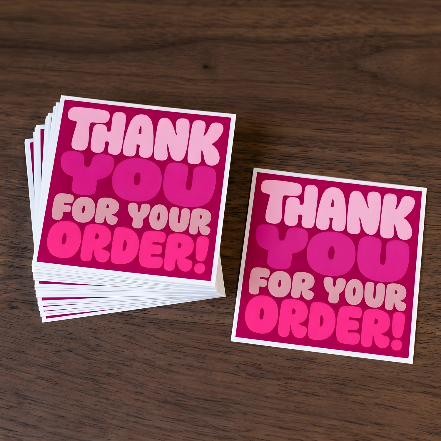 A stack of square thank-you stickers with placed on a dark wood surface, alongside one individual sticker.