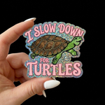 Custom sparkling glitter sticker with a turtle and text 'I SLOW DOWN FOR TURTLES' held by a hand against a black background