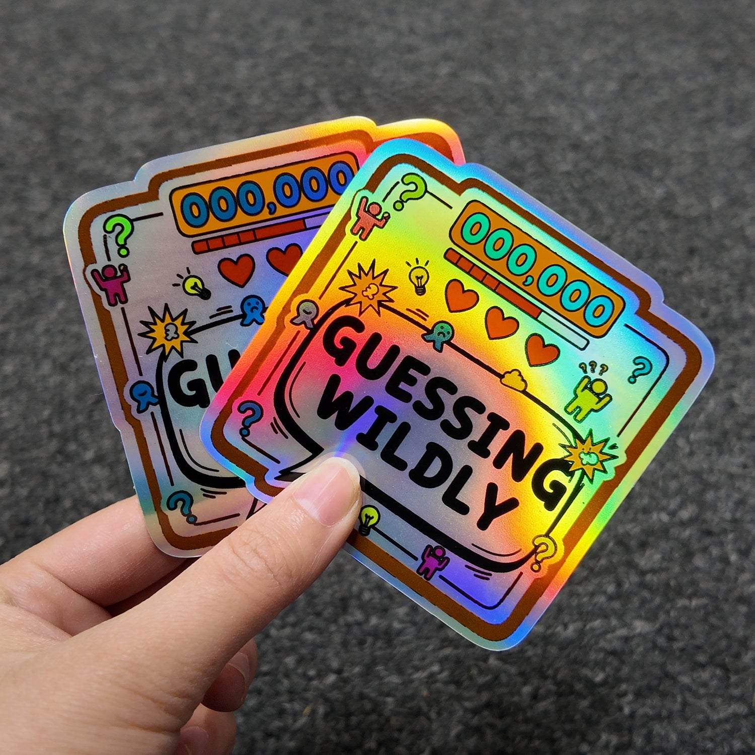 Holographic stickers with 'Guessing Wildly' text held by a hand against a dark background