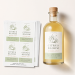 Stack of premium waterproof vinyl sheet labels next to a glass bottle of Citrus Bloom botanical syrup.