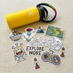 A variety of weatherproof custom glossy stickers, including mountains and robots, spread next to a yellow dishwasher safe water bottle.
