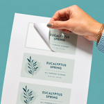 A hand peeling a weatherproof vinyl label for Eucalyptus Spring all-purpose cleaner from a sticker sheet.