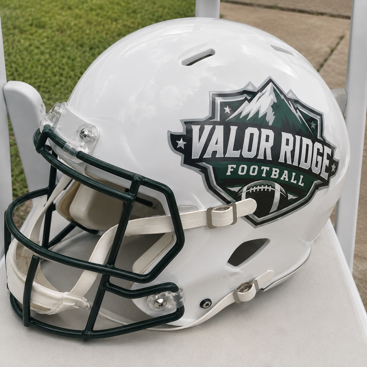Close-up of a white football helmet with a dark green facemask, featuring a custom Valor Ridge Football mountain crest decal on the side.