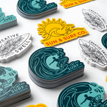 Bulk stacks of colorful custom die-cut stickers in teal, yellow, and white designs.