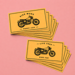 Yellow rectangle stickers with motorcycle illustration stacked on a pink background